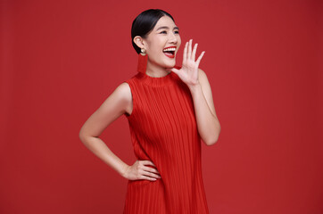 Happy Asian woman wearing red dress with open mouths raising hands shouting announcement isolated...
