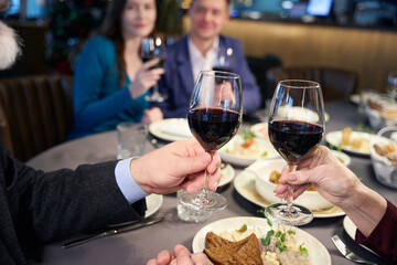 People hands holding glasses with wine while celebrating Christmas