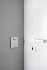 Light switch on gray wall close to white door with metal handle - obrazy, fototapety, plakaty