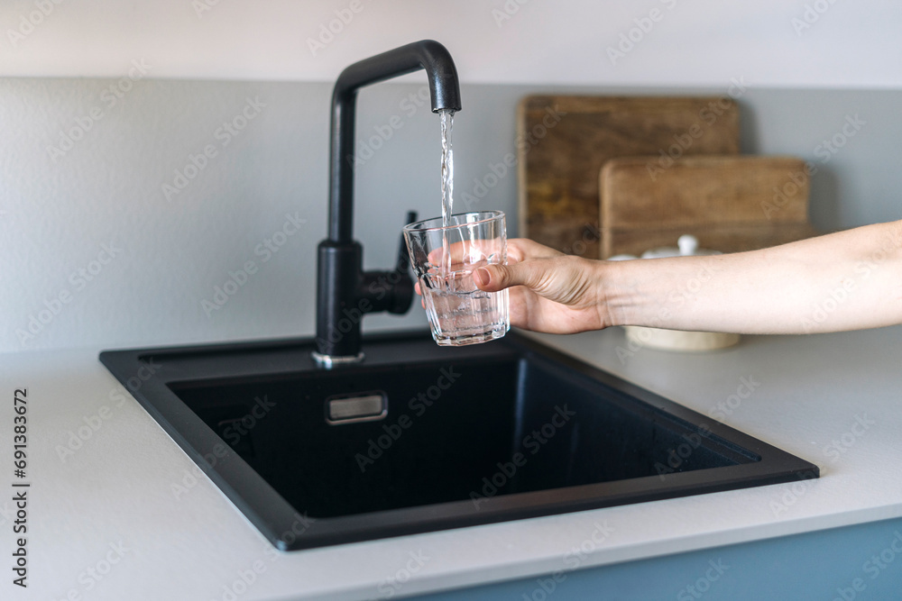 Wall mural selective focus on female hand holding glass and pouring fresh water from faucet