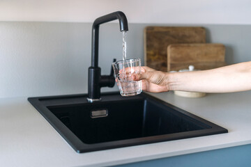 Selective focus on female hand holding glass and pouring fresh water from faucet