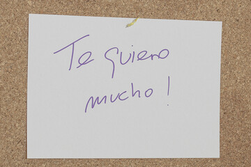 Message written with a pen on a white paper attached to a cork board with the message I love you...
