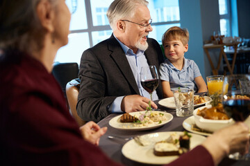 Happy old man and little boy sitting at a festive table in the restaurant