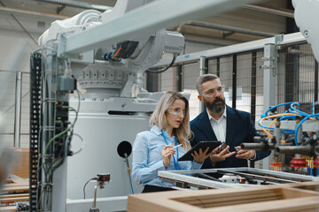 Female engineer and male project manager standing in modern industrial factory by precision robotic...