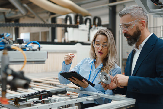 Female engineer and male project manager standing in modern industrial factory by precision robotic arm. Manufacturing facility with robotics, robotic arms, automation and industrial robotic