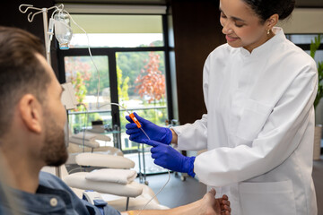 Nurse or doctor making vitamin IV infusion drip for male patient in hospital or beauty salon.
