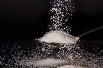 Close-up of refined sugar raining on a spoon, black background, diabetic concept, with copy space