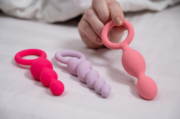A woman chooses anal beads from a set while lying in bed. 