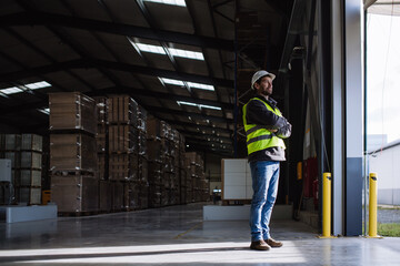 Portrait of warehouse worker taking break from work, standing and looking outdoors. Worker in reflective clothes, with copy space. - obrazy, fototapety, plakaty