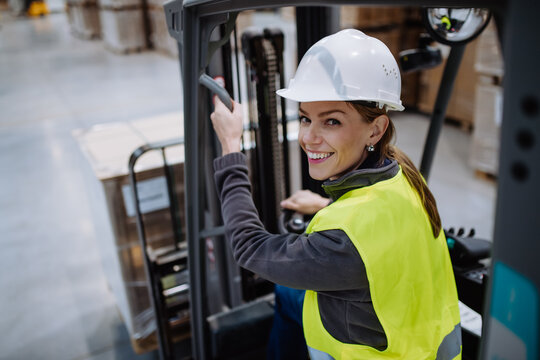 Female warehouse worker driving forklift. Warehouse worker preparing products for shipmennt, delivery, checking stock in warehouse.