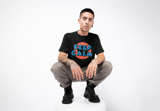 Mockup of man wearing customizable t-shirt crouching on plinth