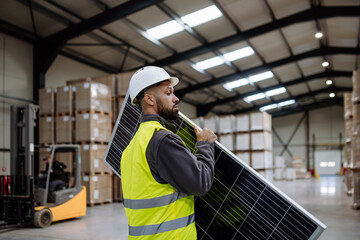 Handsome worker carrying solar panel in warehouse, factory. Solar panel manufacturer, solar manufacturing.
