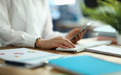 Female hands hold smartphone and work on laptop keyboard. Mobile applications for business and...