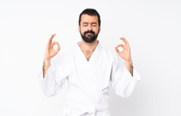 Naklejka premium Young man doing karate over isolated white background in zen pose