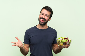 Young handsome man with salad over isolated green wall smiling