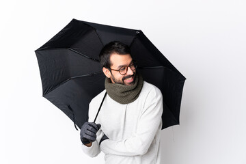 Caucasian handsome man with beard holding an umbrella over isolated white wall with arms crossed and happy