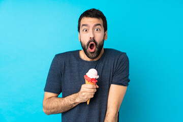 Young man with a cornet ice cream over isolated blue background with surprise facial expression