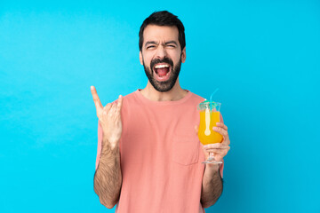 Young man over holding a cocktail over isolated blue background making rock gesture