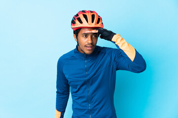Young cyclist man with braids over isolated background looking far away with hand to look something