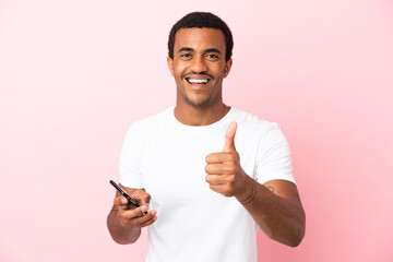 African American handsome man on isolated pink background using mobile phone while doing thumbs up