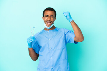 African American dentist holding tools over isolated blue background celebrating a victory