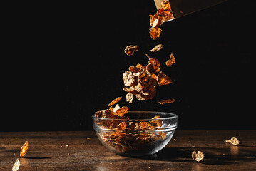 Cornflakes sprinkle on a bowl on black background