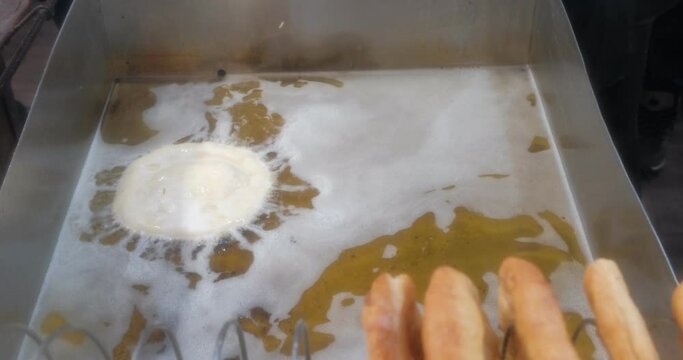 Turkish pisi (deep-fried dough) is cooking in oil in frying pan on the stove