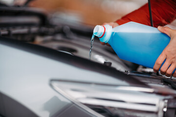 Pouring winter washer fluid into car reservoir during winter, protecting it from freezing. - obrazy, fototapety, plakaty