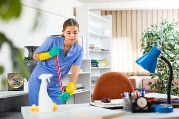 Hardworking young woman from a cleaning company carefully conducts a wet cleaning of the office