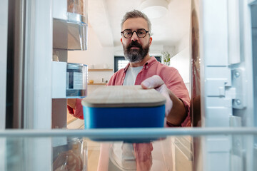 Handsome man putting lunchbox in fridge. Taking out lunch from fridge, eating leftovers. Stop...