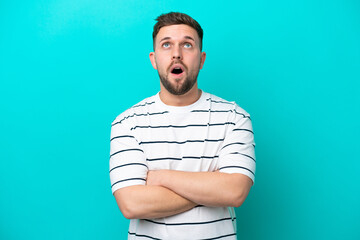 Young caucasian man isolated on blue background looking up and with surprised expression