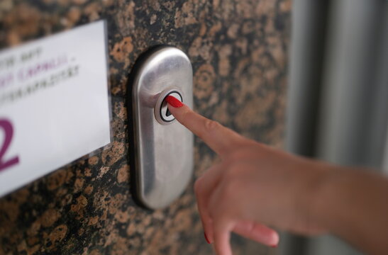 Female finger with red manicure pressing elevator button closeup. Elevator service and repair concept