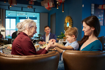 Overjoyed aged woman with little boy while celebrating New Year in restaurant