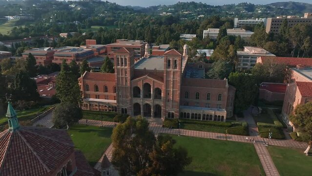Aerial view of UCLA campus with Royce Hall center stage, Romanesque architecture, green spaces, and Westwood's urban backdrop in golden morning - afternoon light.