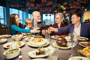 Fototapeta na wymiar Joyful family clinking glasses at Christmas party in cozy festively restaurant