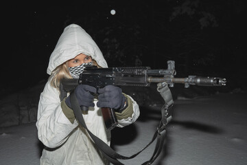 A girl soldier in winter camouflage takes aim with an AK 12 assault rifle, close-up photo.