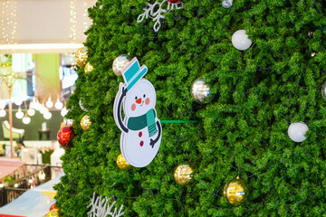 Toy snowman in a hat and scarf with a bell on a New Year tree.