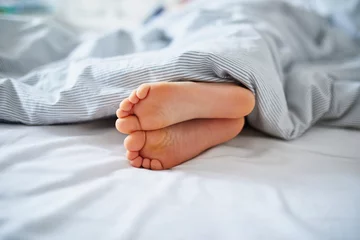 Fotobehang Little child's feet in bed covered with blanket © Ekaterina Pokrovsky