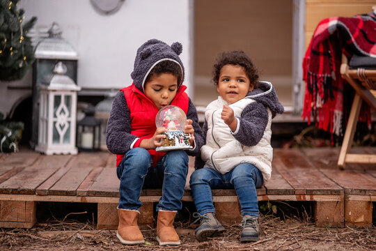 African American boy and girl are sitting on wooden pallets, playing with a Christmas snow globe