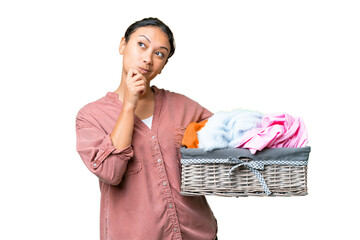 Young Uruguayan woman holding a clothes basket over isolated chroma key background having doubts