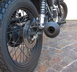 Macro ruota posteriore con freno a disco argentato e marmitta nera opaco di moto classica cafe race