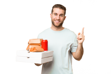 Young handsome blonde man holding pizzas and burgers over isolated background showing and lifting a finger in sign of the best