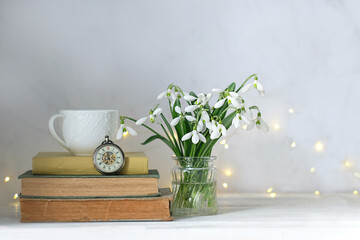 Snowdrop flowers, vintage pocket watch clock, cup and books on table close up. spring background. Blossoming snowdrops, symbol of spring season. Relaxation, reading time