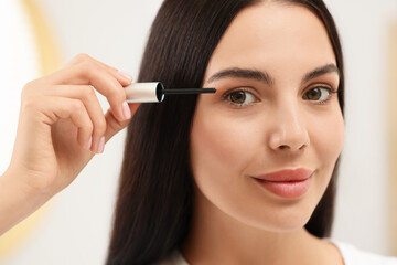 Beautiful woman applying serum onto her eyelashes indoors, closeup. Cosmetic product