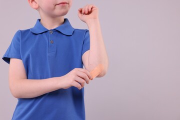Little boy putting sticking plaster onto elbow against light grey background, closeup. Space for...