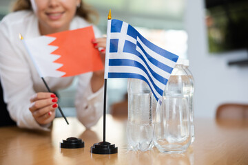 Young female assistant setting up greek and bahraini flags for international negotiations