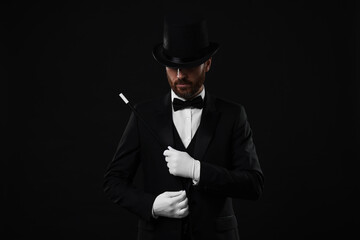 Magician in top hat holding wand on black background