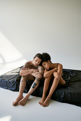 good looking young multiracial couple in underwear sitting close to each other on bed, togetherness