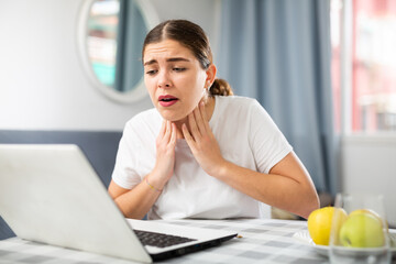 Young girl sitting at a table in front of a laptop in an apartment informs the doctor at the...