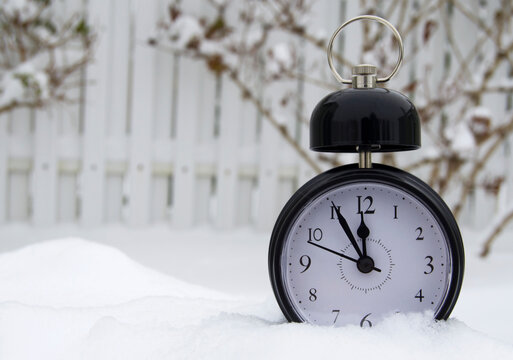 Black alarm clock on white snow background. Clock shows time 11:55. 5 minutes left until the New Year. Christmas concept.